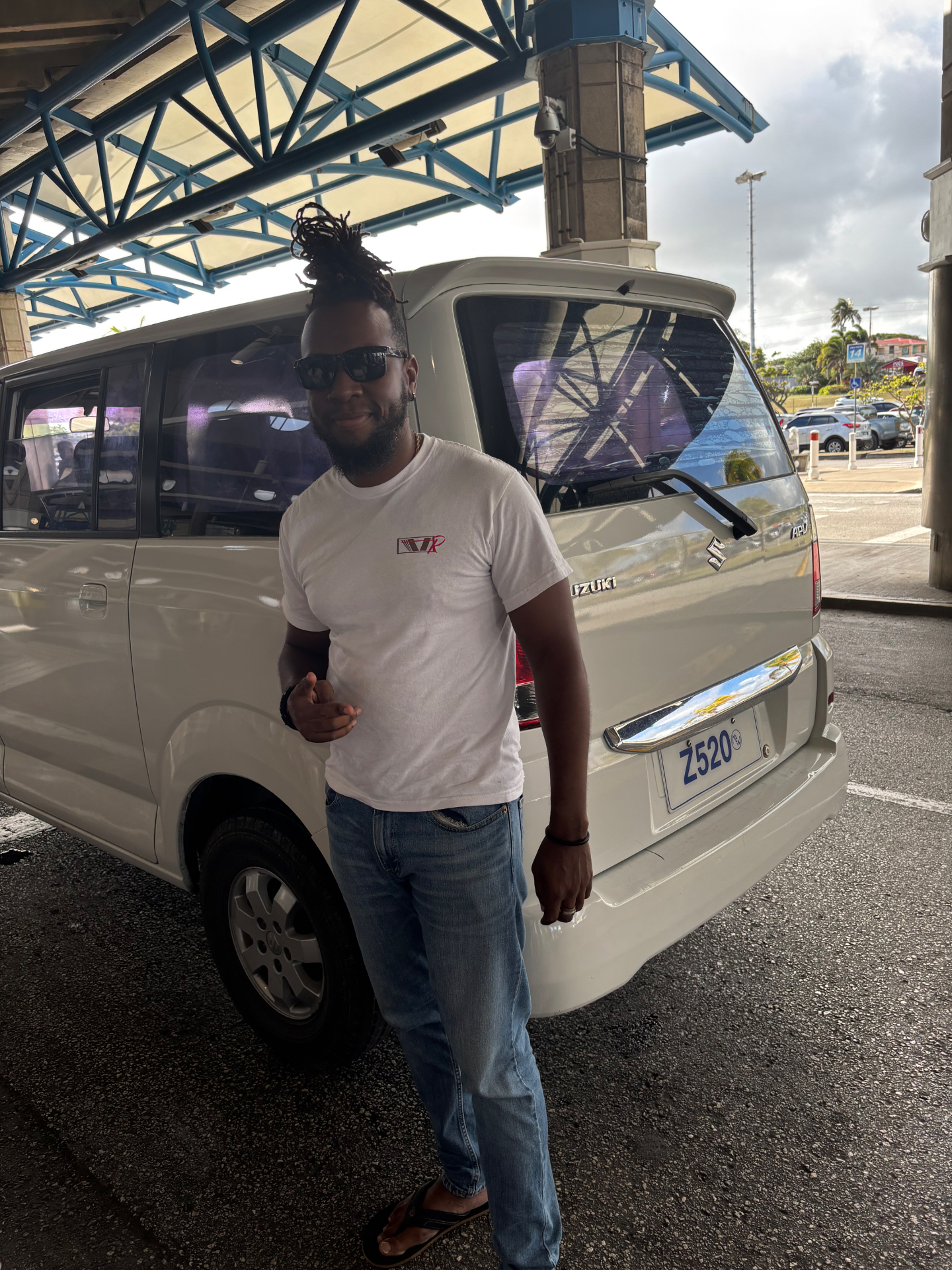 A local driver smiling beside his van outside the airport terminal in Barbados